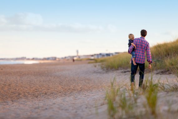 Junger Vater mit Kind auf dem Arm läuft an einem Strand